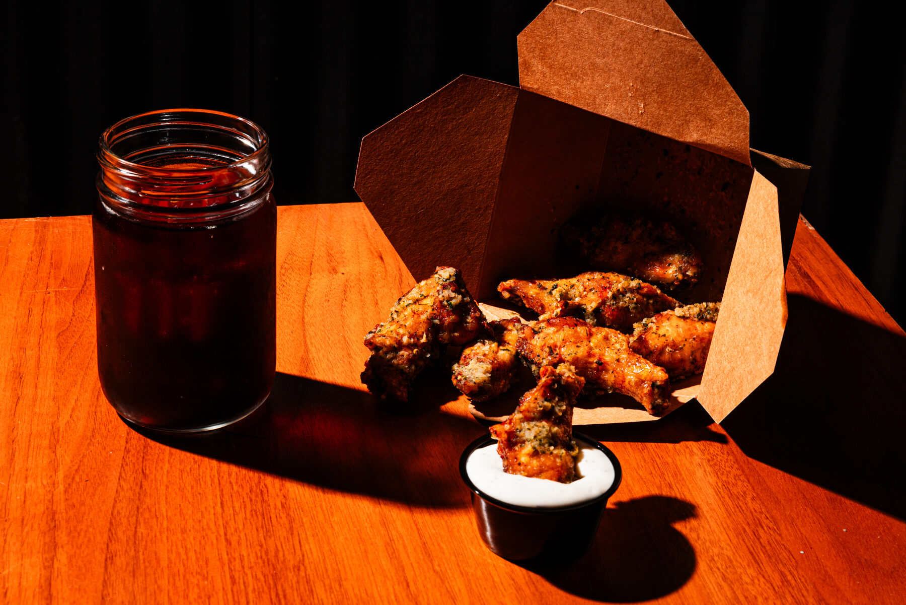 Garlic lemon pepper wings spilling from a kraft takeout box, one wing dipped in ranch, warm cinematic light